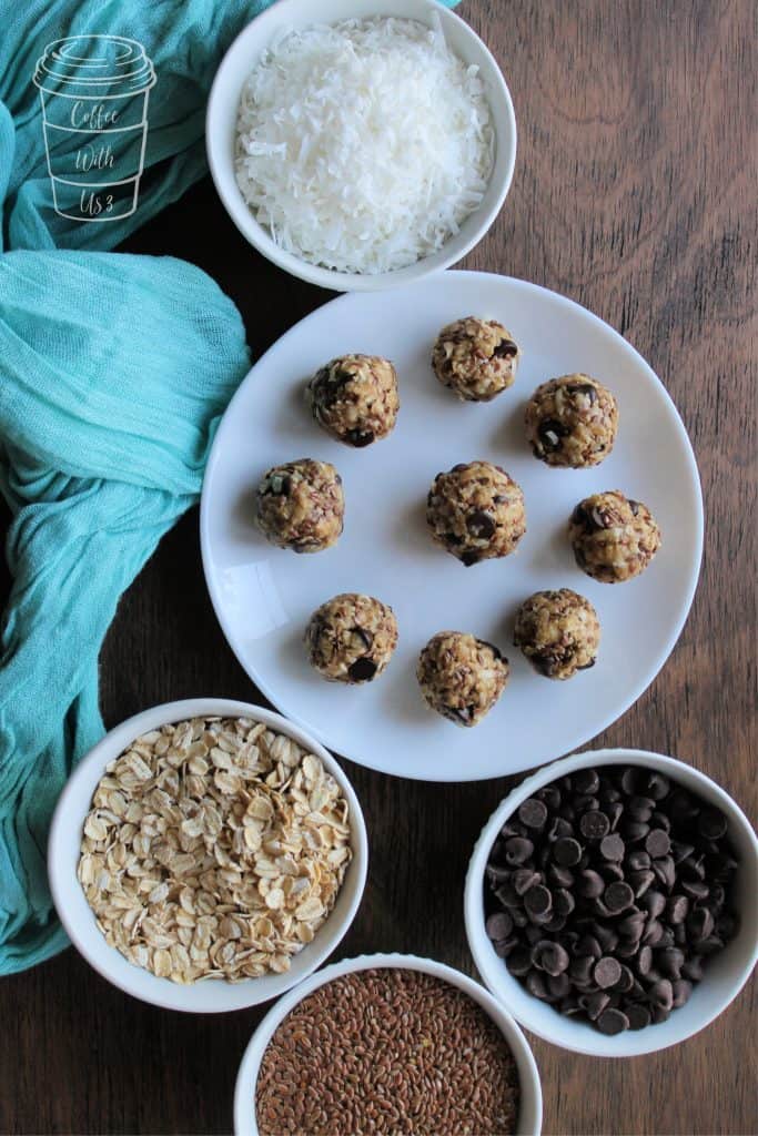 Overhead shot of granola bites on a white plate, surrounded by white bowls full of oats, coconut, flax seed, and chocolate chips.