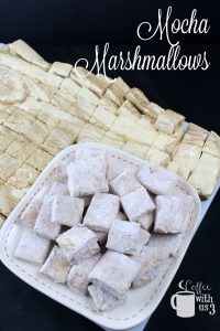 Mocha marshmallows cut and dusted on a plate with undusted marshmallows in the background.