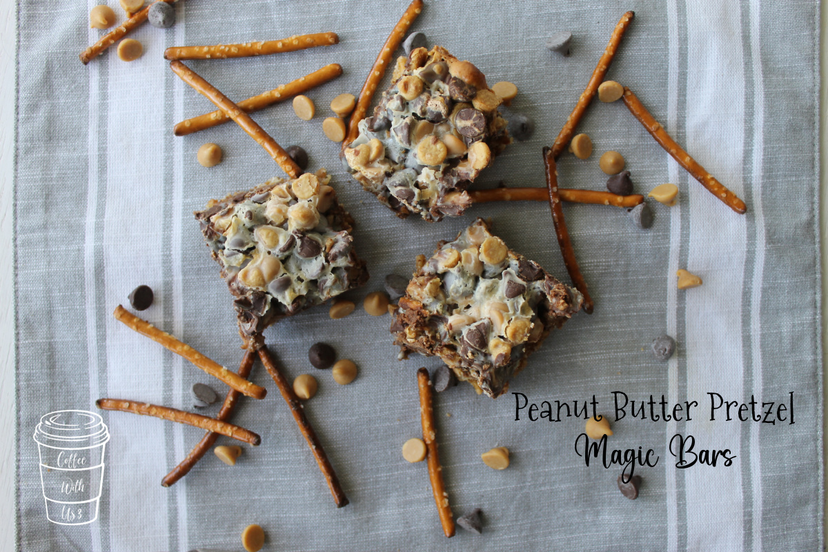 Three square Peanut Butter Pretzel Magic Bars over a grey linen background with pretzels and chocolate chips scattered about